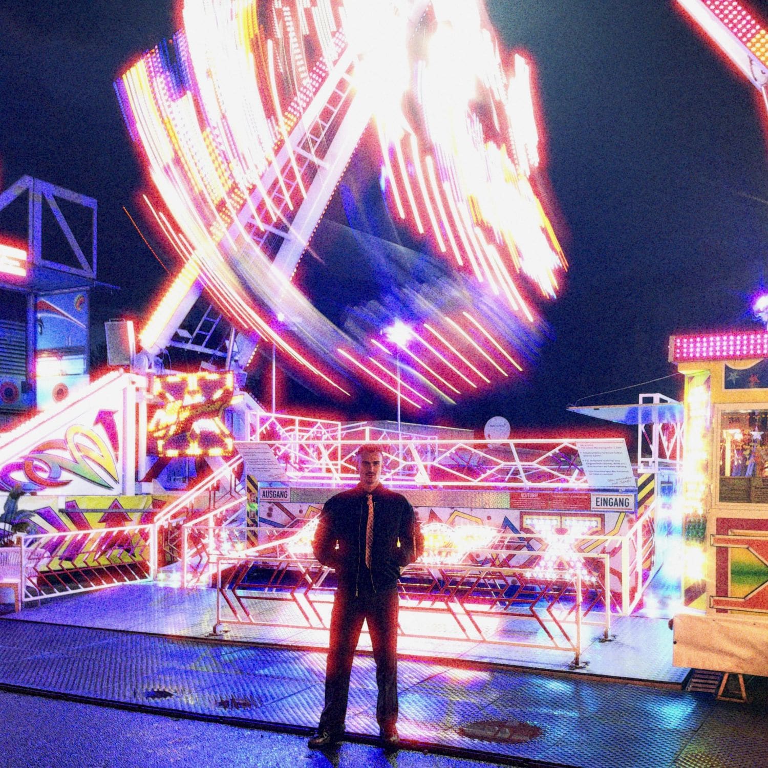 Yan Vom Weltraum standing in front of a spinning fairground ride at night